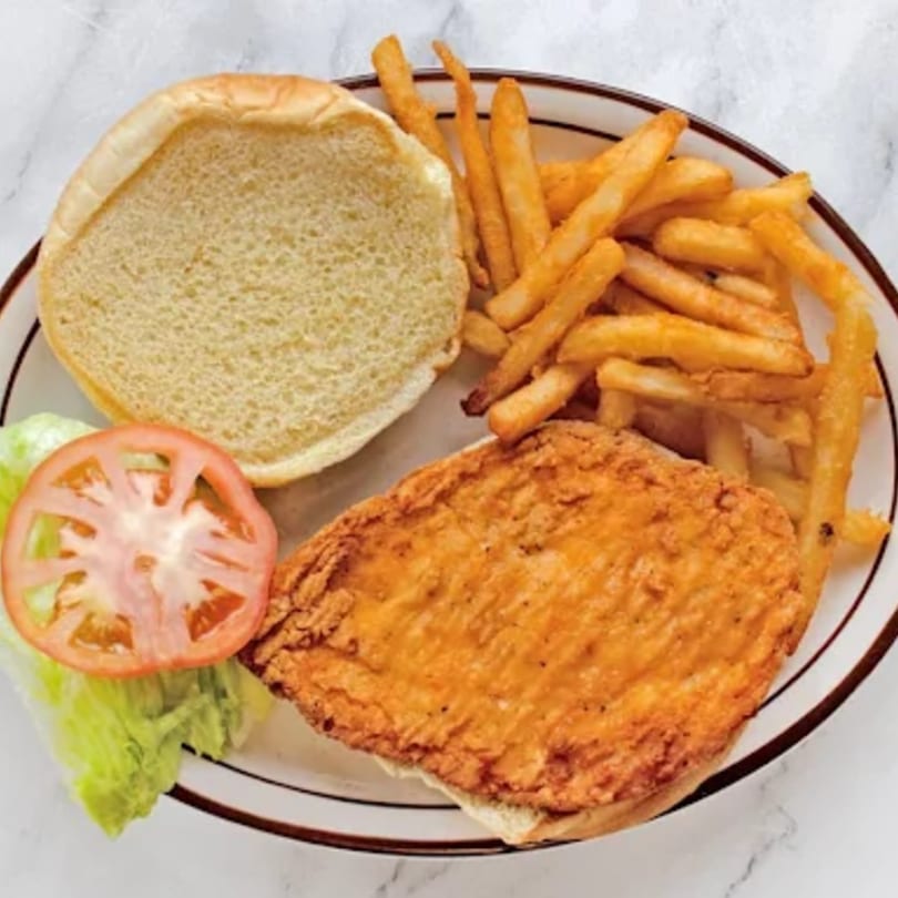 A fried chicken sandwich with lettuce, tomato, and a side of french fries on a white plate.