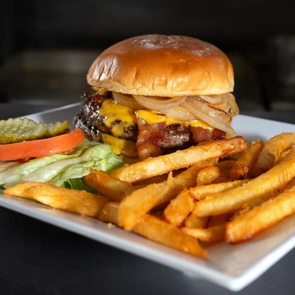 A cheeseburger with bacon, caramelized onions, and fries, served with a side salad.