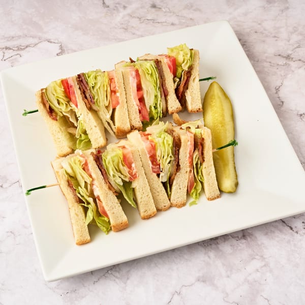 Two club sandwiches, each cut into halves, with a pickle spear on a white rectangular plate.